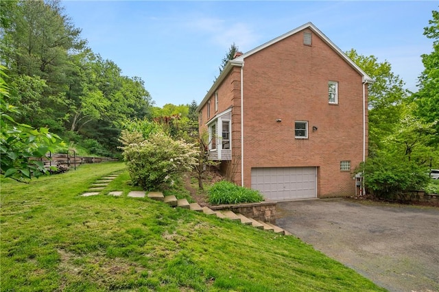 view of property exterior featuring brick siding, a garage, asphalt driveway, and a lawn