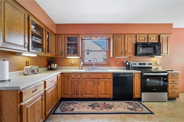 kitchen featuring black appliances, a sink, light countertops, glass insert cabinets, and brown cabinets