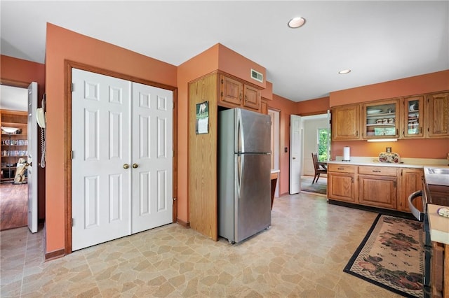 kitchen with freestanding refrigerator, light countertops, glass insert cabinets, stone finish flooring, and recessed lighting