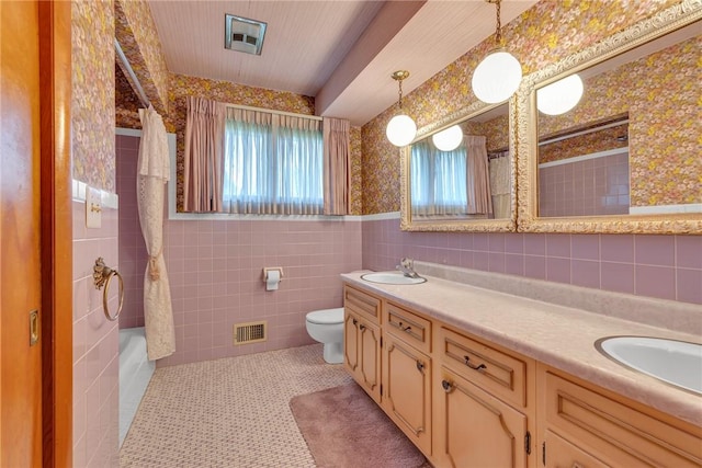 full bath with tile walls, toilet, double vanity, wallpapered walls, and shower / bathtub combination with curtain