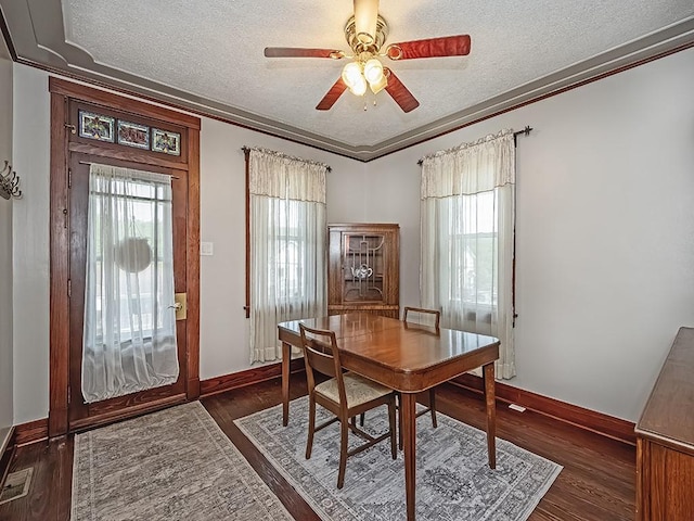 dining space featuring a textured ceiling, ornamental molding, a ceiling fan, baseboards, and dark wood finished floors