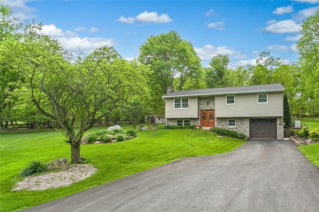 raised ranch with an attached garage, driveway, a chimney, a front lawn, and view of wooded area