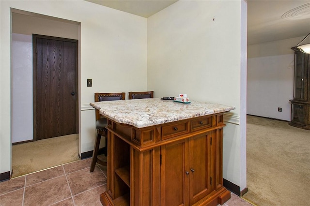 kitchen featuring carpet floors, brown cabinets, light stone counters, and baseboards