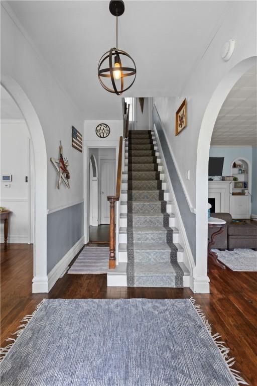 staircase with wood finished floors, arched walkways, and baseboards