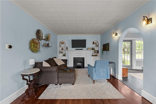 living area featuring ornamental molding, built in features, dark wood-type flooring, a fireplace with flush hearth, and baseboards