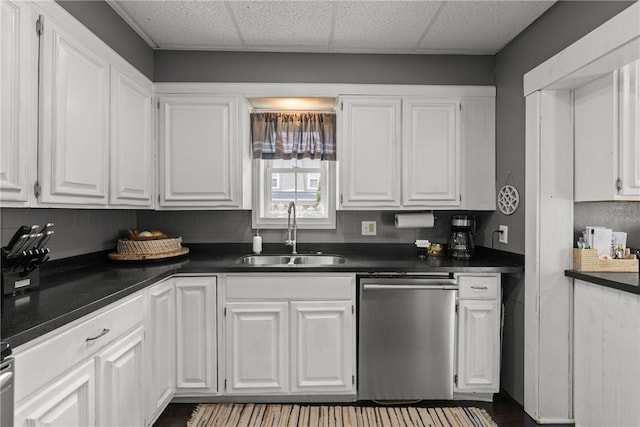 kitchen featuring a sink, dishwasher, dark countertops, white cabinetry, and a drop ceiling