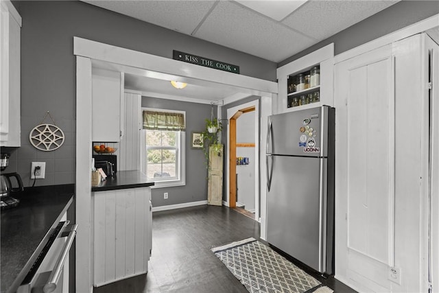 kitchen featuring freestanding refrigerator, dark countertops, backsplash, dark wood finished floors, and white cabinetry