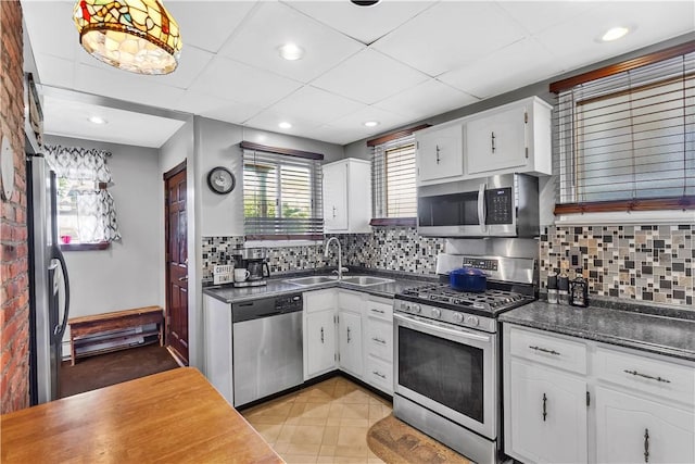 kitchen with stainless steel appliances, a sink, dark countertops, white cabinetry, and decorative backsplash