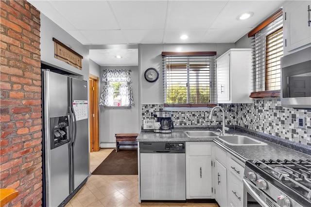 kitchen with appliances with stainless steel finishes, a sink, white cabinets, dark countertops, and a baseboard heating unit