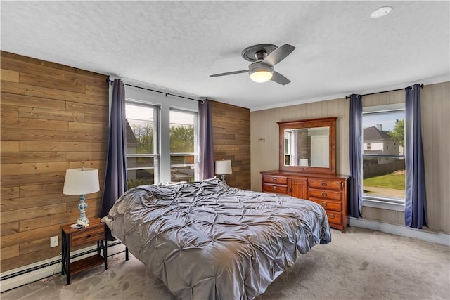 bedroom featuring a baseboard heating unit, wood walls, light colored carpet, a textured ceiling, and ceiling fan