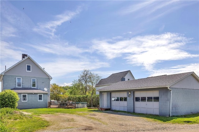 view of property exterior featuring a detached garage, an outdoor structure, and a shingled roof