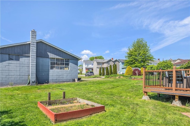 view of grassy yard with a vegetable garden, a deck, and a residential view