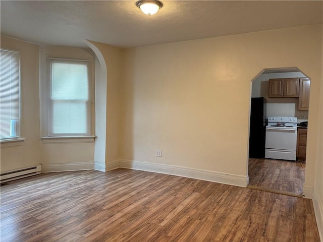 spare room with wood finished floors, arched walkways, a baseboard heating unit, and baseboards