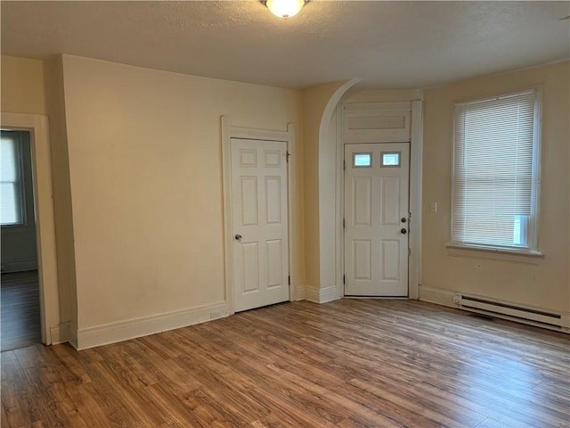 foyer with arched walkways, wood finished floors, healthy amount of natural light, and baseboards
