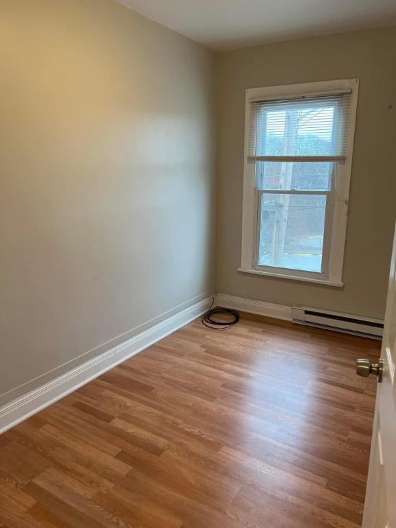 empty room featuring baseboard heating, wood finished floors, and baseboards