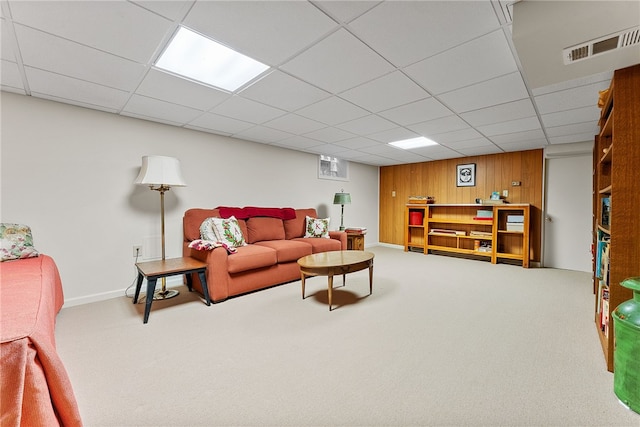 carpeted living room with wood walls and a drop ceiling