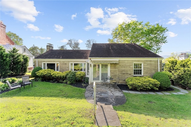 view of front of home with a front lawn, stone siding, a chimney, a patio, and a shingled roof