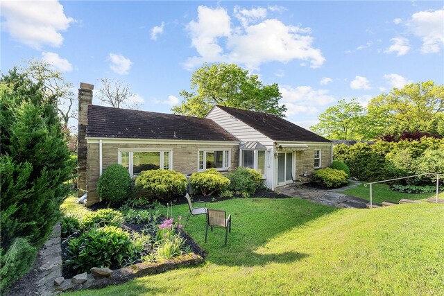 rear view of property featuring stone siding, a yard, and a chimney