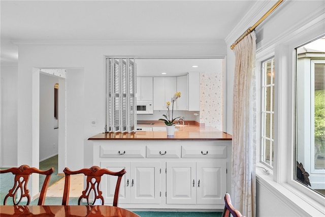 kitchen featuring white microwave, ornamental molding, white cabinets, baseboards, and decorative backsplash