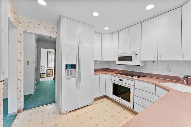 kitchen with white appliances, a sink, white cabinetry, light flooring, and wallpapered walls
