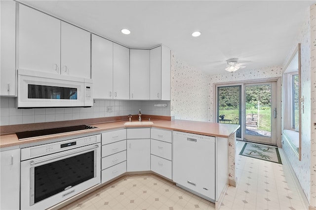 kitchen featuring white appliances, a sink, a peninsula, white cabinetry, and wallpapered walls