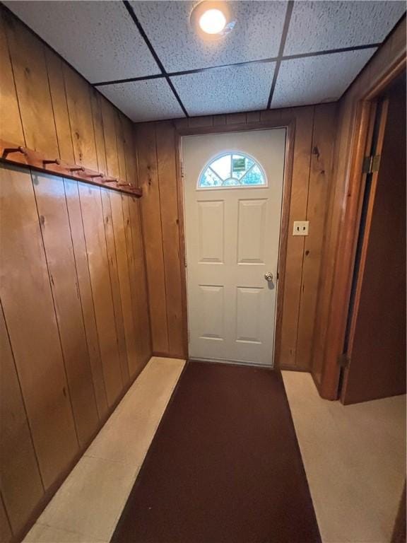 entryway with a paneled ceiling, wooden walls, and dark colored carpet