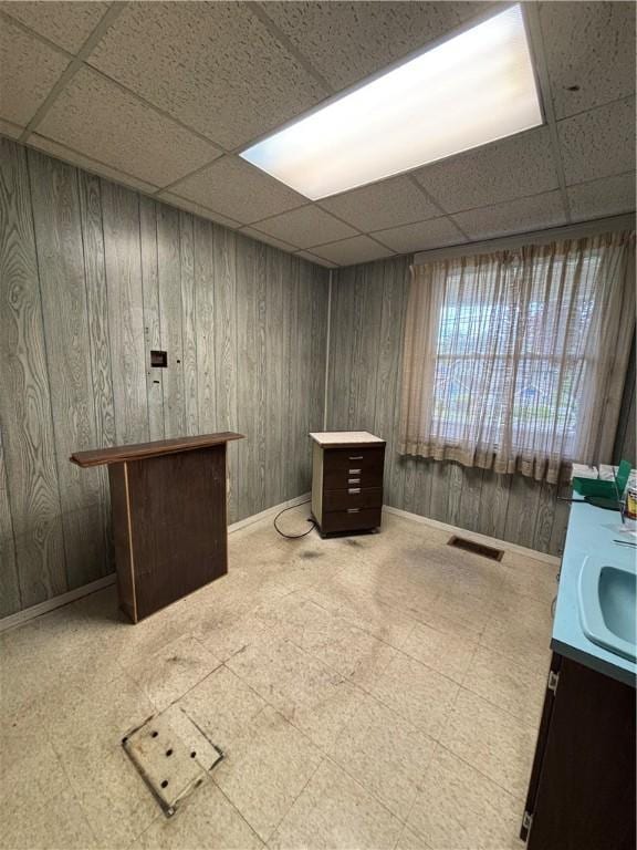 misc room with a drop ceiling, tile patterned floors, wooden walls, baseboards, and a sink