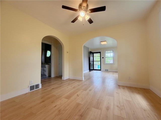 unfurnished room featuring light wood-type flooring, arched walkways, a ceiling fan, and baseboards