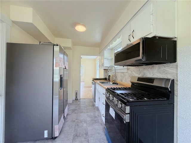kitchen with stainless steel appliances, a sink, tasteful backsplash, and white cabinets