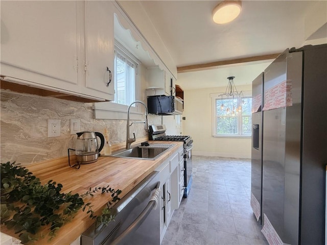 kitchen with appliances with stainless steel finishes, a sink, backsplash, white cabinetry, and healthy amount of natural light