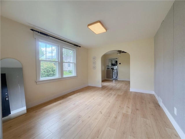 unfurnished room featuring arched walkways, light wood-type flooring, and baseboards