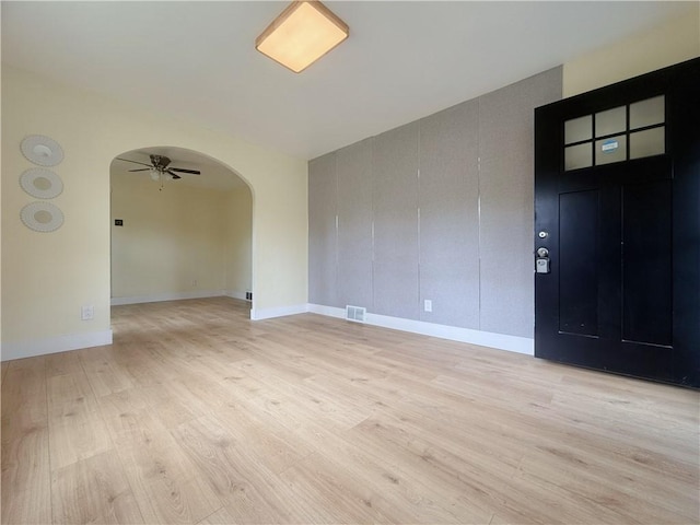 spare room featuring arched walkways, light wood-type flooring, ceiling fan, and baseboards