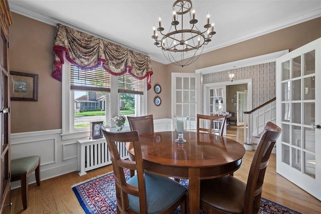 dining space featuring a wainscoted wall, wood finished floors, ornamental molding, a chandelier, and french doors