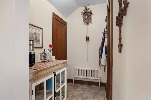hallway featuring lofted ceiling, stone finish flooring, and baseboards