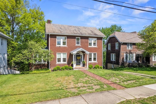 colonial-style house with a chimney, a front yard, and brick siding