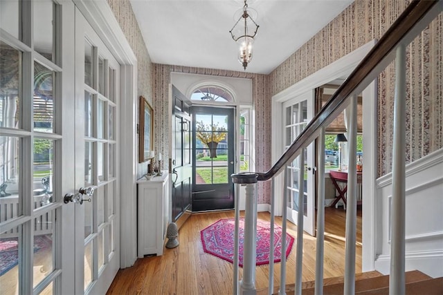 entryway with wallpapered walls, french doors, a chandelier, and wood finished floors