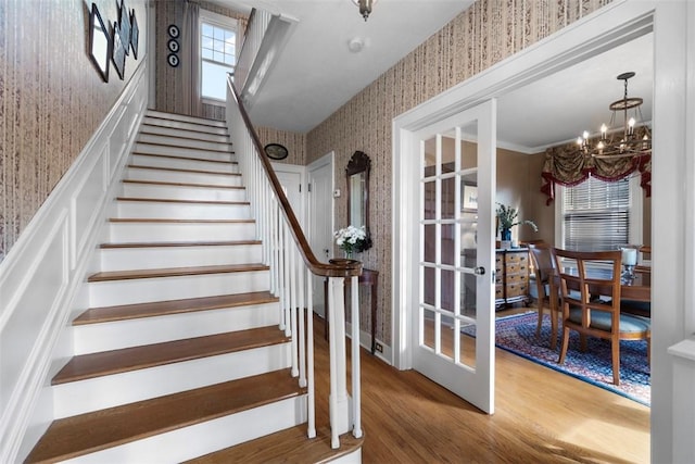staircase featuring wallpapered walls, wood finished floors, a chandelier, and healthy amount of natural light
