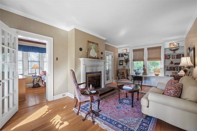 living room with a glass covered fireplace, light wood finished floors, ornamental molding, healthy amount of natural light, and baseboards