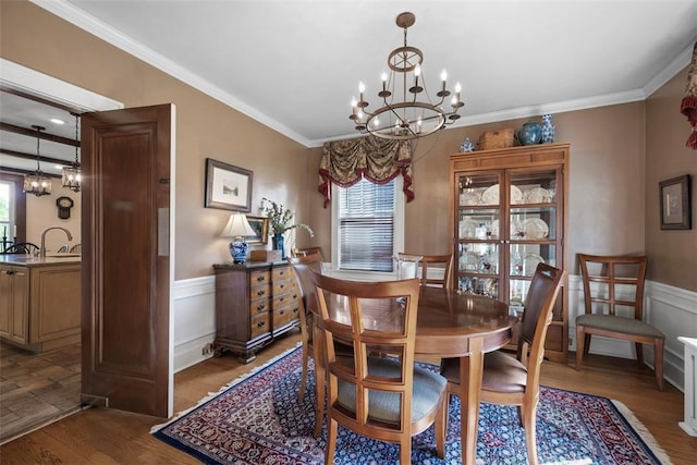 dining area featuring a chandelier, wood finished floors, a wainscoted wall, and ornamental molding