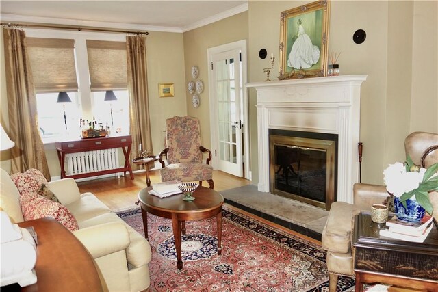 living area featuring wood finished floors, ornamental molding, a glass covered fireplace, and radiator heating unit