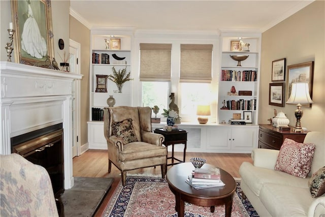 living area with light wood-style floors, crown molding, built in features, and a glass covered fireplace