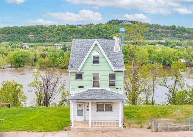 victorian house featuring a shingled roof, a chimney, a water view, and fence