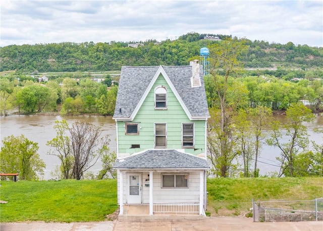 victorian house featuring a shingled roof, a chimney, a water view, and fence