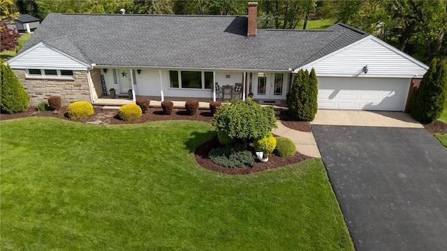 view of front facade with a chimney, asphalt driveway, a front yard, a garage, and covered porch