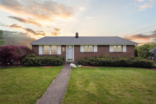 view of front of home with brick siding, a lawn, and a chimney
