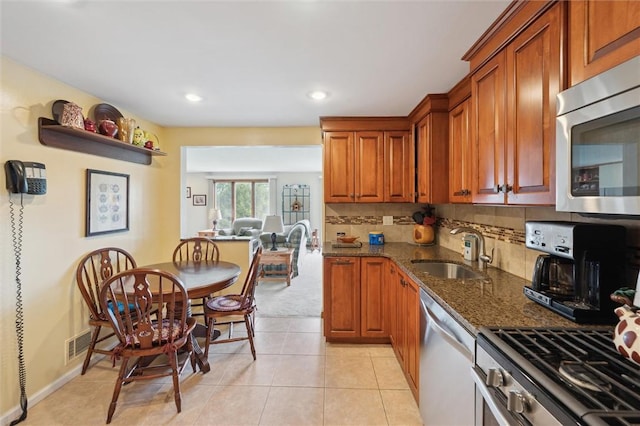 kitchen with appliances with stainless steel finishes, a sink, dark stone counters, brown cabinets, and backsplash