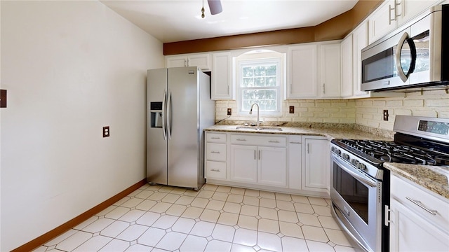 kitchen with appliances with stainless steel finishes, a sink, decorative backsplash, white cabinetry, and light stone countertops
