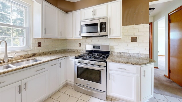 kitchen featuring stainless steel appliances, a sink, white cabinetry, and light stone counters