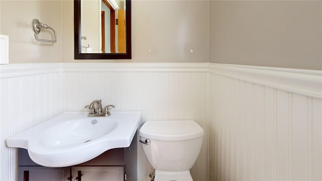 half bath with a wainscoted wall, toilet, and vanity