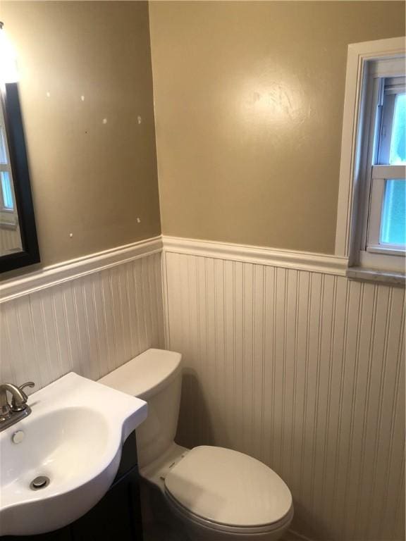 half bath featuring wainscoting, toilet, and vanity